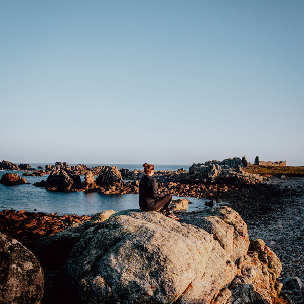 Femme assise sur un rocher en bord de mer en Bretagne