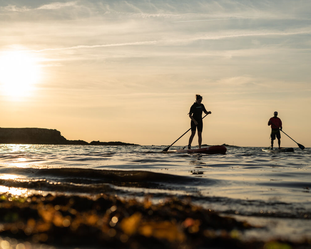Deux personnes faisant du paddle sur la mer au coucher de soleil pour visiter le Finistère