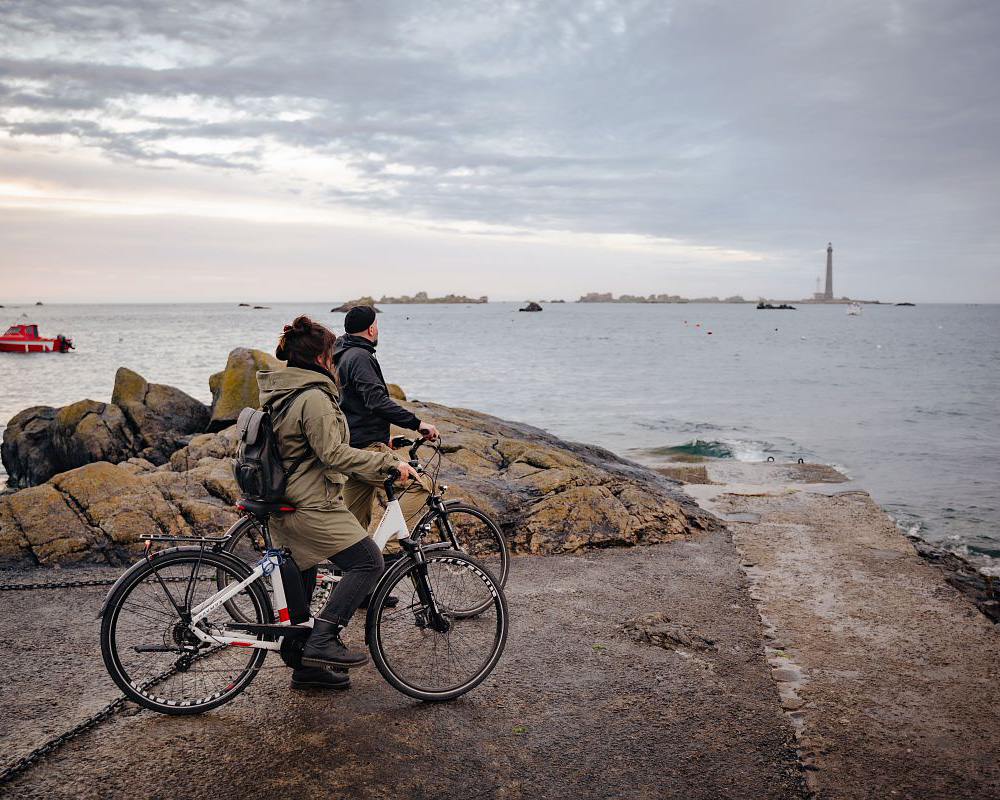 Homme et femme à vélo en bord de mer qui visitent le Finistère
