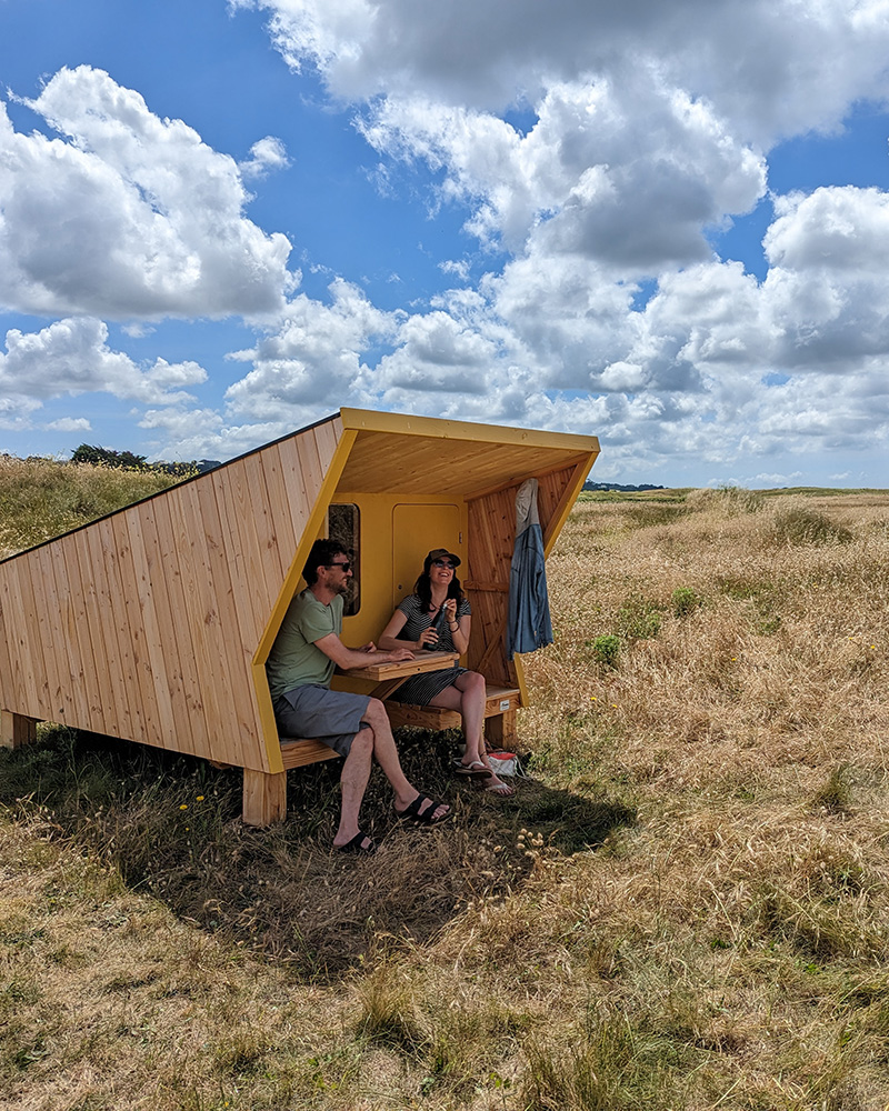Couple de randonneur attablé devant une cabane en bois d'un camping dans le Finistère nord